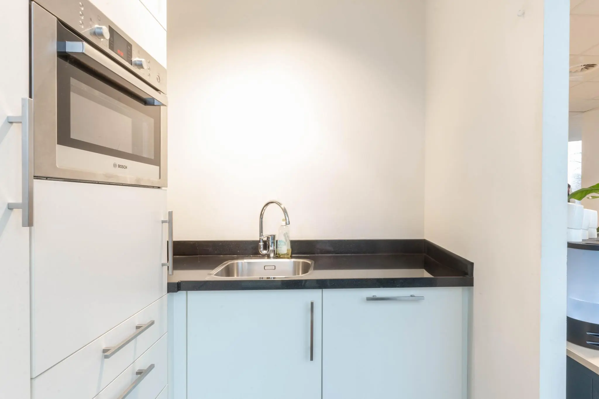 Kleine kitchenette met een ingebouwde Bosch oven, rvs-spoelbak en wit aanrechtblad in een modern interieur aan de 1e Hogeweg.